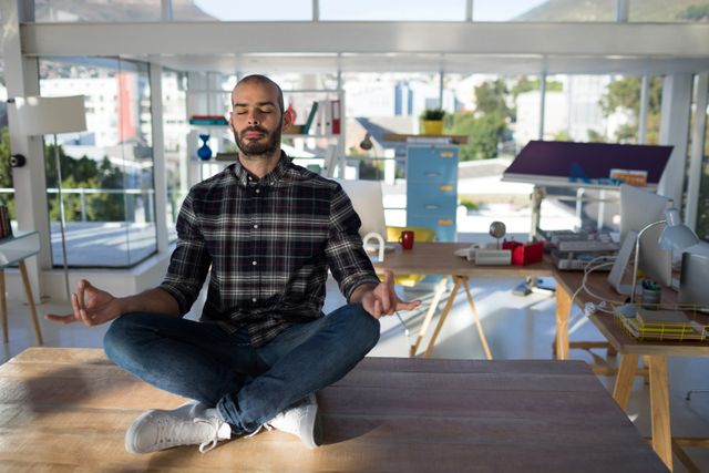 Male executive practicing yoga on office desk in modern workspace. Ideal for illustrating workplace wellness, stress relief, and mindfulness in professional settings. Useful for articles, blogs, and promotional materials on mental health, corporate wellness programs, and productivity tips.