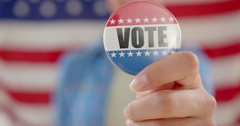 Close-up of hand holding vote badge against american flag