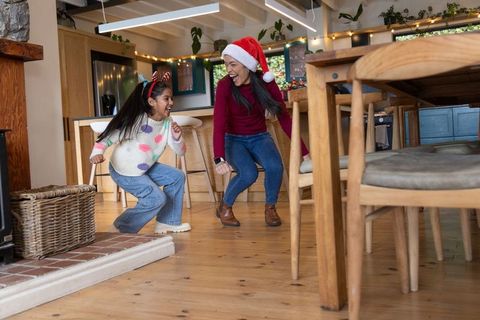 Mother and daughter laughing and playing in cozy kitchen wearing santa hat and antlers