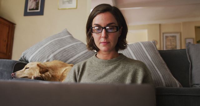 Woman working from home on laptop with dog resting on couch - Download Free Stock Images Pikwizard.com