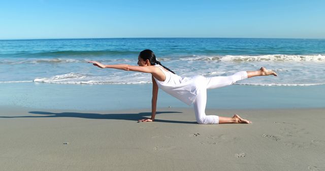 Woman practicing yoga poses on sandy beach with ocean waves in background. Ideal for use in health and wellness promotions, fitness blogs, and relaxation guides.