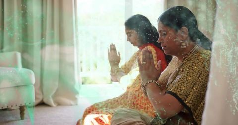 Indian mother and daughter praying by window wearing sari and jewelry, tradition and devotion