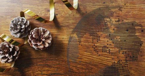 Frosted pine cones with metallic gold ribbon on rustic wooden table with dotted globe