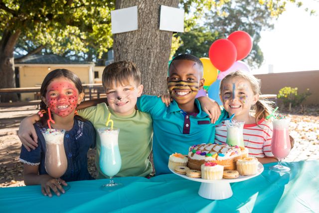 Portrait of smiling children with face paint having food and drinks at park