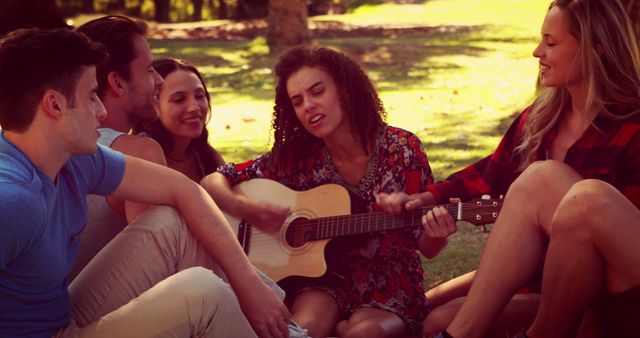 Group of diverse friends sitting on grass in a park, enjoying acoustic guitar performance. Perfect for use in marketing materials for outdoor events, advertisements focused on community and friendship, music-related promotions, and lifestyle blogs.