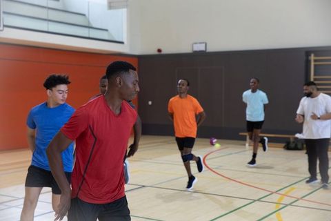 Diverse male athletes performing lateral agility drills on indoor court with volleyball