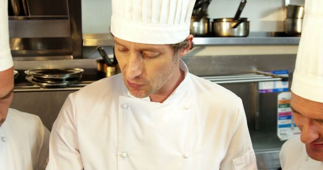 Three professional chefs stand in a commercial kitchen wearing uniforms and chef hats. This can be used in articles or advertisements related to culinary schools, restaurant business, or cooking workshops. Ideal for showcasing teamwork in gastronomy and professional food preparation.