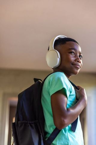 Confident african american boy wearing headphones and backpack standing in hallway