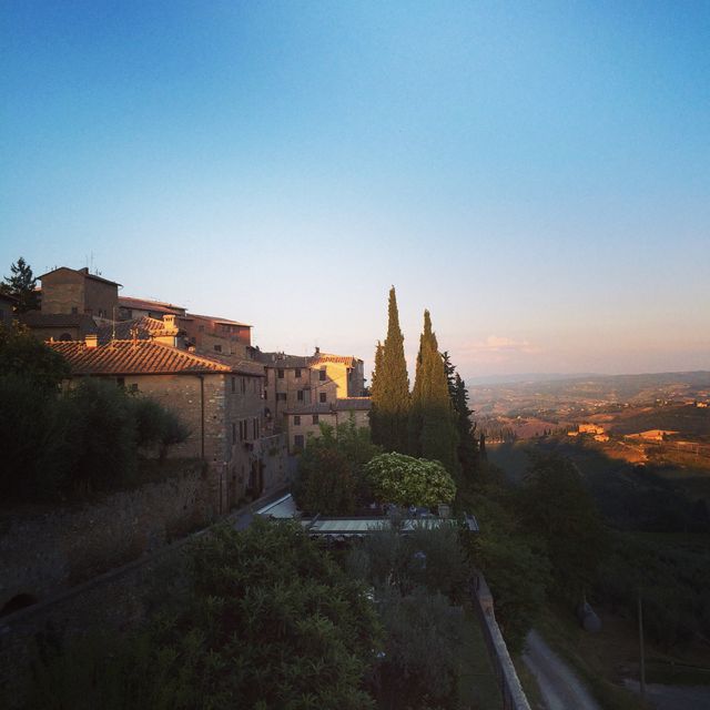 This photo captures a tranquil Tuscan village during sunset with stunning rolling hills in the background. Picture perfect for travel and tourism promotions, blogs about Italian countryside, or artwork reflecting serene, rustic landscapes. Ideal for illustrating themes of peace, rural lifestyle, historic charm, and natural beauty.
