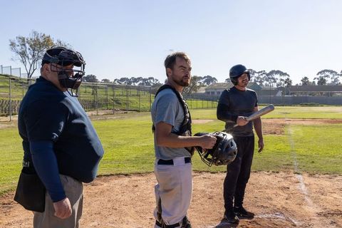 Umpire nodding while catcher holding helmet and batter adjusting bat at home plate
