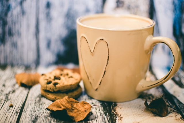 This image features a warm cup of coffee with a heart design on a wooden table accompanied by cookies and autumn leaves. Perfect for illustrating cozy autumn mornings, seasonal decor, or a comforting coffee break. It can be used in lifestyle blogs, seasonal promotions, coffee advertisements, or home decor magazines.