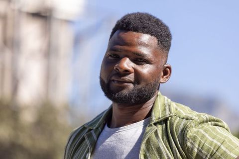 Confident african man wearing green striped overshirt smiling in sunlit urban portrait