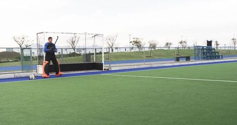 Field hockey goalkeeper in protective gear with stick on field