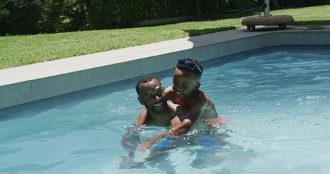 African american father and son playing laughing splashing in backyard pool on sunny day