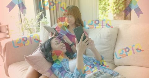 Young women relaxing on couch using smartphone and tablet with colorful lgbt pride ribbon overlay