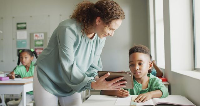 Image of happy caucasian female teacher explaining lesson on tablet to african american boy. school education and teaching profession.