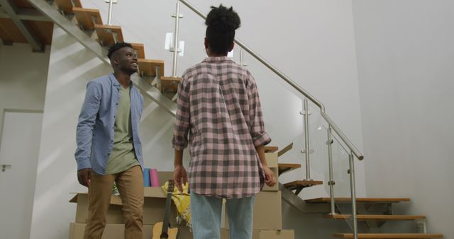 Young couple unpacking in their new home with a staircase in the background. They are surrounded by cardboard boxes. Perfect for themes related to moving in, new beginnings, homeownership, teamwork, and couple activities.