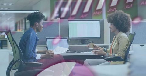 Two women reviewing documents and collaborating at modern open-plan office desk with laptop