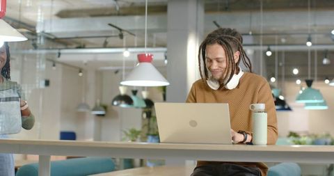 African American man with dreadlocks working on laptop in coworking space with headphones