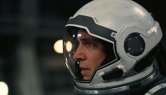 Staring helmeted astronaut scanning cockpit controls in weathered spacesuit closeup profile