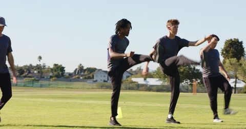 Diverse male athletes marching and high-kicking through cone drill on grassy field
