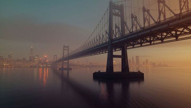 Sunset over iconic suspended bridge and city skyline reflections