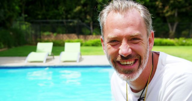 Mature man smiling while enjoying a sunny day by the swimming pool. Could be used in advertisements for summer vacation, wellness retreats, lifestyle blogs, or health and happiness newsletters.