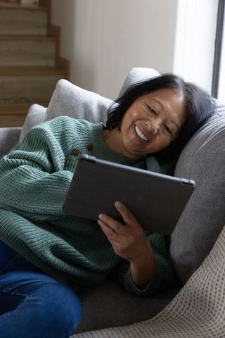 Senior woman smiling while using tablet on comfortable couch