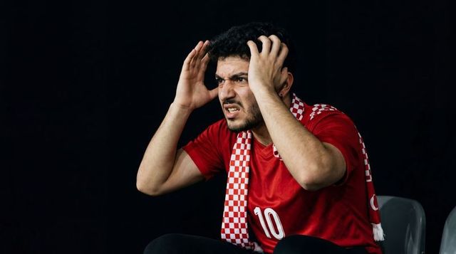 Frustrated soccer fan wearing red #10 jersey clutching head while watching tense match