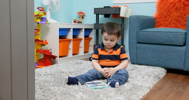 Young boy sitting on comfortable rug playing with tablet. Surroundings include a blue couch, colorful storage bins, and toys. Useful for themes involving childhood, indoor play, modern home lifestyle, use of technology, and relaxed environments.