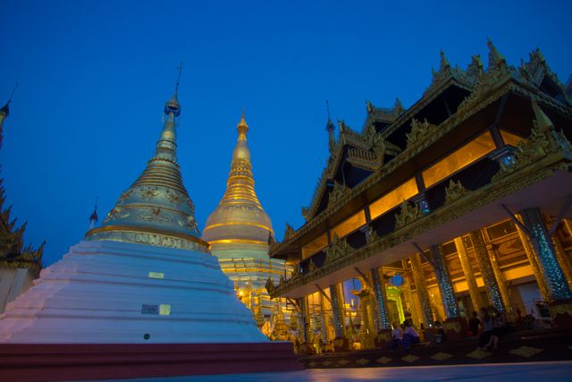 A view of Shwedagon Pagoda at dusk in Yangon, Myanmar featuring illuminated golden stupas and detailed traditional architecture. This image can be used in travel guides, tourism advertisements, cultural blogs, and content highlighting historic and spiritual landmarks of Myanmar.