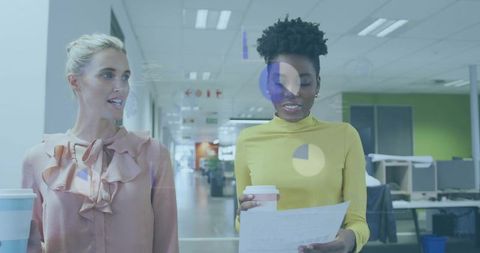 Coworkers walking while holding coffee and discussing documents in modern open-plan office