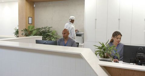 African American clinic reception team working at modern front desk in grey scrubs