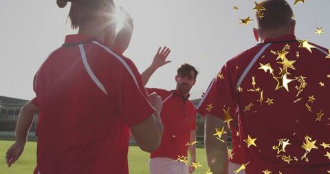 Backlit team celebrating after match waving teammates in red jerseys on grass field