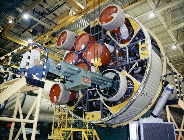 Workers at the Michoud Assembly Facility near New Orleans, Louisiana, are installing an engine on the S-IB stage. The S-IB stage, developed by Marshall Space Flight Center and produced by Chrysler Corporation, features eight H-1 engines for a combined thrust of 1,600,000 pounds. This image can be used to depict rocket science, engineering, spaceflight history, manufacturing processes, and the aerospace industry.