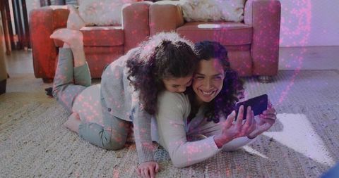 Mother daughter lying on rug sharing smartphone moments cozy living room bonding