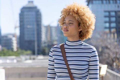 African american woman looking confident on urban terrace wearing striped top and brown bag