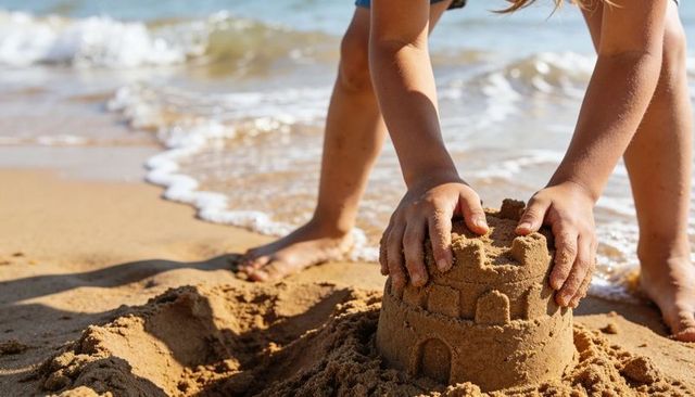 Child building sandcastle on sunny shoreline hands shaping turret waves lapping summer
