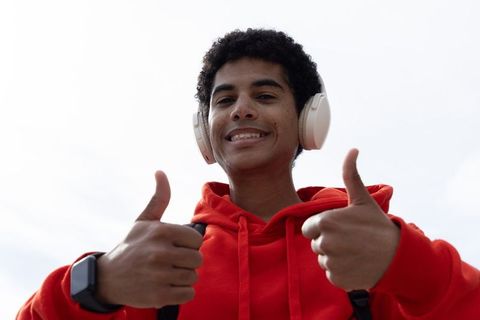 African american teen smiling and giving thumbs up while wearing headphones and red hoodie