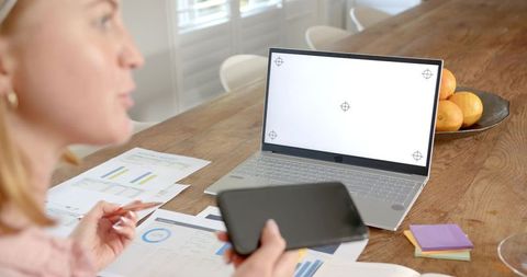 Woman studying charts at home with laptop and smartphone for remote work and productivity