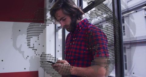 Checking smartphone by glass wall with dotted globe decal, bearded man in red-blue shirt