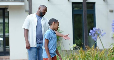African american father teaching son about garden plants while pointing at purple flowers