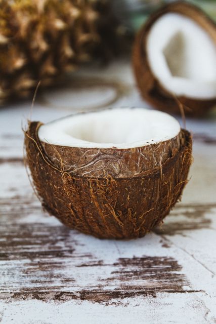 Halved coconut resting on rustic wooden surface. Suitable for tropical themes, healthy lifestyle promotions, organic food advertising, and natural product displays. Useful for recipes, blogs, and wellness-related content.