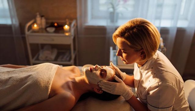 Esthetician applying facial mask during candlelit spa treatment promoting relaxation