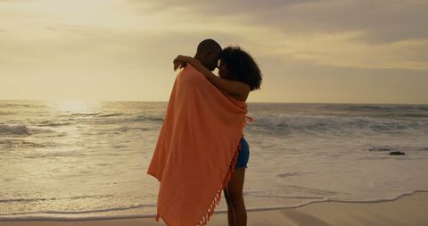Romantic Couple Embraces Under Blanket at Sunset Beach