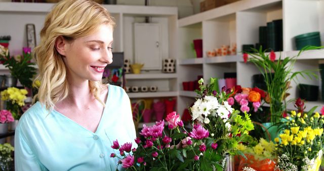 Female florist arranging bouquets of colorful flowers in flower shop. Smiling while working, wearing a casual light blue shirt. Ideal for promotions of floristry businesses, small business advertisements, spring and summer themes, and professional occupation contexts.