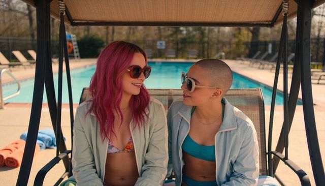 Poolside friends chatting on shaded swing wearing sunglasses and summer swimwear