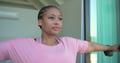 African american woman exercising with dumbbell on balcony wearing pink workout top