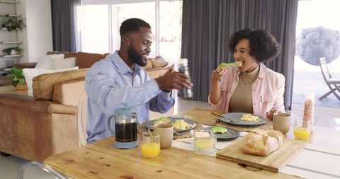 Mid-adult couple enjoying sunlit breakfast in open-plan living room with avocado toast