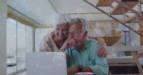Senior couple using laptop with global network overlay in sunlit modern home interior